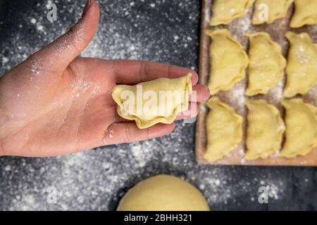 Knödel in Mehl auf dem Holzbrett, Hand halten varenik vor dem Kochen. Ukrainische traditionelle Küche Stockfoto