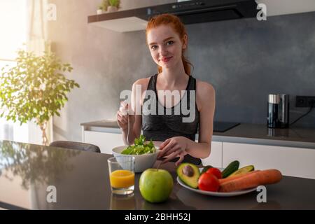 Athletisches Mädchen mit Turnkleidung isst einen Salat in der Küche Stockfoto
