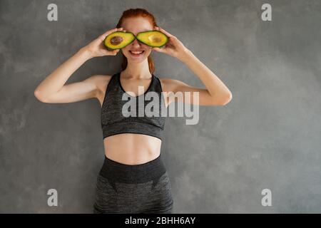 Athletisches Mädchen mit Turnkleidung isst Avocado zu Hause. Stockfoto