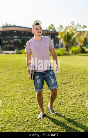 Junger Mann, der mit Laptop unterwegs ist, während er im Park sitzt Stockfoto