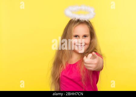 Porträt von positiven glücklichen kleinen Mädchen mit langen Haar und Engel Halo Zeigefinger, die Wahl und Blick auf die Kamera mit toothy Lächeln. In Stockfoto