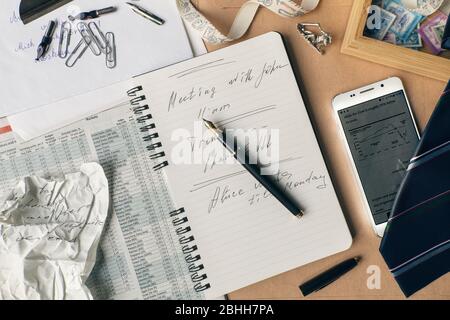 Öffnen Sie Notizbuch mit Notizen auf der Seite, ein zerknittert Blatt Papier, Handy mit einer Aktie, Business-Magazin und Briefpapier?n den Schreibtisch. Stockfoto