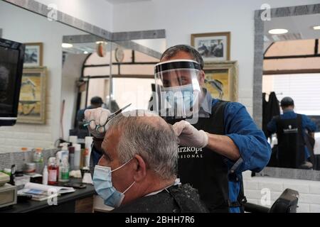 Ein israelischer Friseur trägt Schutzmaske und Gesichtsschutz aufgrund der COVID-19 Coronavirus Pandemie, die die Haare des Kunden in einem Friseurladen in West Jerusalem Israel schneidet Stockfoto