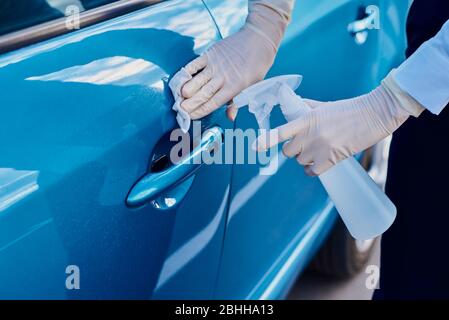 Frau desinfiziert Autotürgriff mit einem antibakteriellen Spray. Autowäsche Stockfoto