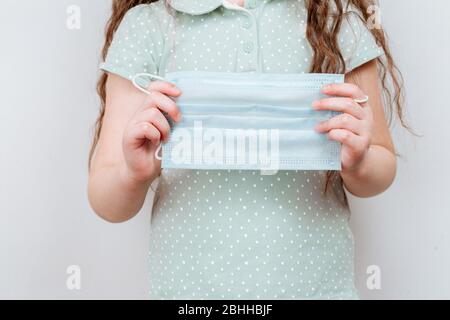 Ein Mädchen hält eine medizinische Maske in den Händen. Coronavirus Pandemie. Antivirale medizinische Maske zum Schutz vor Grippeerkrankungen. Stockfoto