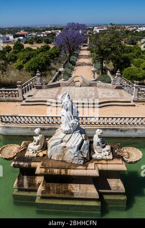 Estoi, Portugal - 15. Juni 2018 Brunnen mit Statuen im Garten des Palastes. Straße in der Mitte zwischen Bäumen. Linie des Horizonts. Leuchtendes Blau sk Stockfoto