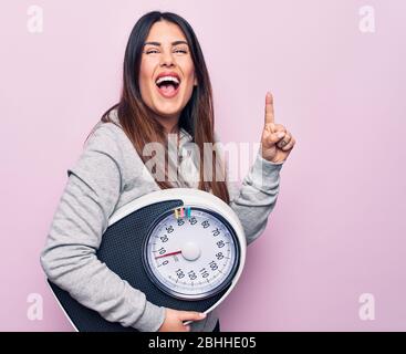 Junge schöne brünette sportliche Frau Kontrolle Gewicht mit Gewichtmaschine lächeln mit einer Idee oder Frage Zeigen Finger mit glücklichem Gesicht, num Stockfoto