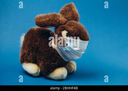 Spielzeughasen stehen in einer medizinischen Maske auf blauem Hintergrund. Konzept des Schutzes vor Atemwegserkrankungen, Virus. Coronavirus stoppen. Stockfoto