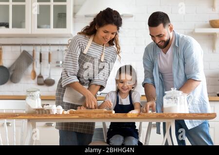 Lächelndes junges Paar lehrt kleine Tochter Kuchen in der Küche backen. Stockfoto