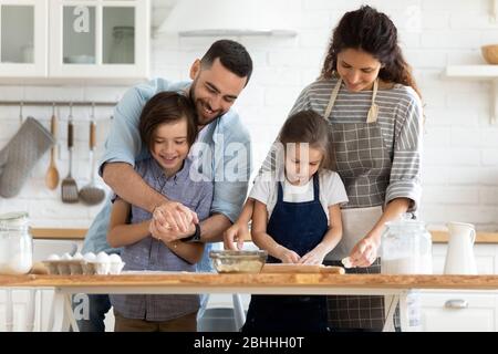 Glücklich Millennial verheirateten Paar Unterricht kleine Kinder machen hausgemachte Gebäck. Stockfoto