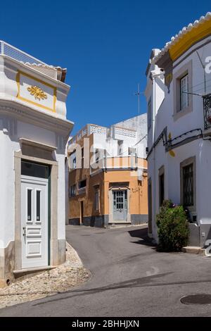 Enge Straße einer Altstadt an einem sonnigen Tag mit blauem Himmel. Häuser mit meist weißer Fassade. Estoi, Portugal. Stockfoto