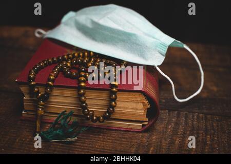 Heiliger Al Quran, Gebetsperlen und Schutzmaske auf Holztisch. Coronavirus Covid-19 Quarantäne muslimische Gebet Konzept. Stockfoto