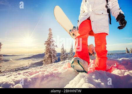 Eine Frau, die das Snowboard in den Händen hält, macht einen Schritt nach vorn. Snowboarding Action Konzept, Sonnenuntergang Licht Stockfoto