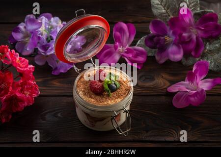 Cremiges Dessert in einem Glas mit Schokoladenstückchen und Beeren auf einem dunklen Holzhintergrund dekoriert Stockfoto