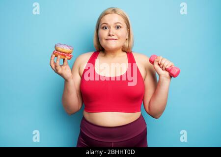 Fette Mädchen denkt, Donuts zu essen statt Turnhalle. Konzept der Unentschlossenheit und des Zweifels Stockfoto