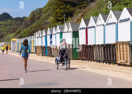 Bournemouth, Dorset, Großbritannien. April 2020. UK Wetter: Schöner warmer sonniger Tag, da die Temperaturen an den Stränden von Bournemouth an der Südküste steigen, während die Menschen ihre erlaubte Bewegung machen, die meisten halten sich an die Coronavirus Richtlinien. Die Strände sind praktisch menschenleer, da Polizei und ratsarbeiter die Gegend patrouillieren. Junge Frau Radfahren entlang der Promenade auf Dreirad vorbei an Strandhütten - Fahrrad Fahrrad Fahrrad Trike Dreirad Radfahrer. Quelle: Carolyn Jenkins/Alamy Live News Stockfoto