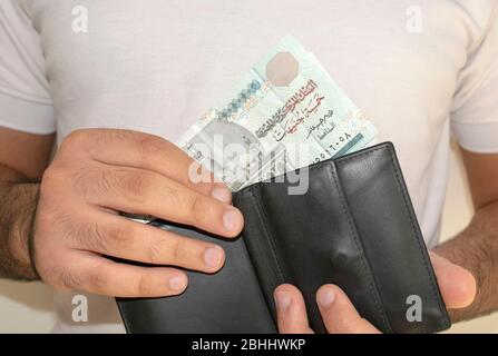 Ägyptens nationale Währung. Geldscheine. Mann im weißen T-Shirt legte ägyptische Pfund-Banknoten in eine schwarze Brieftasche. Ein junger Mann hält in den Händen Geldbörse mit e Stockfoto