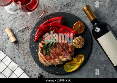 Gehacktes gebratenes Schweinefleisch Steak, Gemüse und Wein auf grauem Hintergrund. Grillgerichte Stockfoto