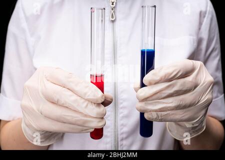 Zwei Fläschchen mit blauer und roter Flüssigkeit, in Handschuhen vor dem Hintergrund eines Arztes. Entwicklung von Impfstoffen und Medikamenten. Medizinische und wissenschaftliche Bio Stockfoto