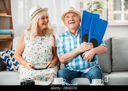 Ältere Paar sitzt in Reisebüro sitzen Hüte Frau mit Schwimmbrille während Mann hält Flossen träumerisch Stockfoto