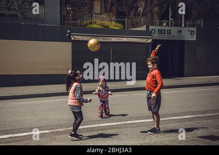 Barcelona, Spanien. April 2020. Ein kleines Mädchen mit einem schützenden Gesicht beobachtet andere Kinder, die mit einem Ball von ihrem Fahrrad vor der Basilika Sagrada Familia in Barcelona spielen, während Spanien die Sperrstunde für unter 14 Jahre erleichtert und ihnen nach sechs Wochen einen einstündigen begleiteten Spaziergang durch die nahe Nachbarschaft gewährt Eine landesweite Sperrung durch die kontinuierliche Ausbreitung des Corona-Virus. Spanien verzeichnete bisher fast 400 neue Todesfälle mit einer Todesrate von fast 23000 Todesfällen. Quelle: Matthias Oesterle/Alamy Live News Stockfoto