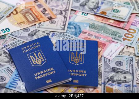 Zwei ukrainische biometrische Pässe liegen vor dem Hintergrund von Währungen aus verschiedenen Ländern der Welt, Euro, Dollar, Griwnja, Forint. Der Stockfoto