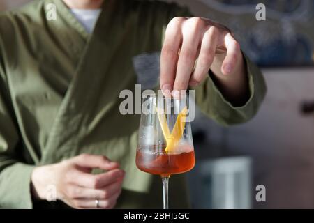 Der männliche Barkeeper gibt Zitronenschale in den Cocktail in Weinglas Stockfoto