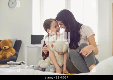 Alles Liebe zum Muttertag. Frohe Familie. Mutter und Tochter umarmen sich, während sie auf dem Bett in einem weißen Zimmer sitzen.
