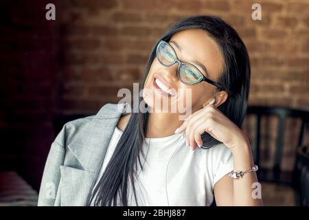 Schöne kaukasische Frau, die im Café lächelnd eine Brille trägt und Musik über Kopfhörer hört. Stockfoto