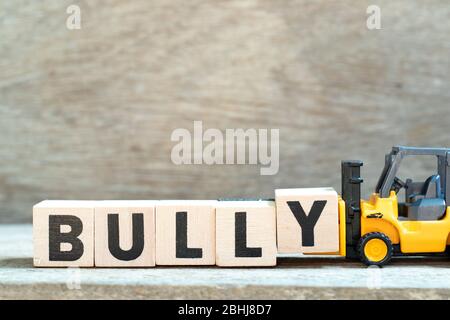Spielzeug Gabelstapler halten Buchstaben Block y Wort Bully auf Holz Hintergrund zu vervollständigen Stockfoto