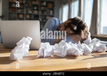 Müde, überarbeiteter Geschäftsmann, der am Schreibtisch schlief, bedeckte zerknitterte Papiere Stockfoto
