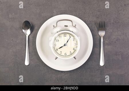 Wecker mit Löffel und Gabel auf dem Teller der Tisch. Zeit zum Essen Stockfoto