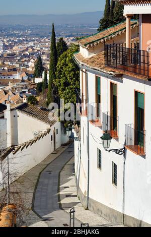 Leere charmante schmale Straße zwischen Wohnhäusern, die bis zu den Bergen der Sierra Nevada führen, hinunter zur Altstadt von Granada Resort Stadt. Sonniger Tag Stockfoto