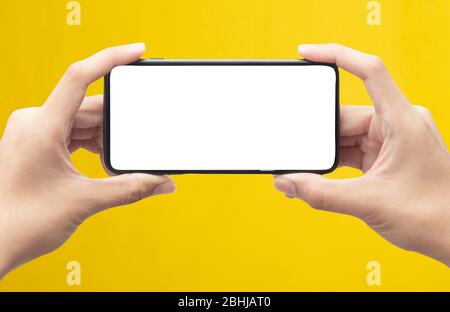 Männliche Hände halten das schwarze Smartphone mit leerem Bildschirm isoliert auf gelbem Hintergrund mit Clipping-Pfad. Stockfoto