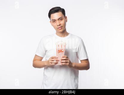 Junger asiatischer Mann in weißem T-Shirt Popcorn hält und Blick auf Kamera und lächelnd isoliert auf weißem Hintergrund. Stockfoto