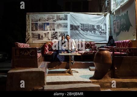 Jeddah / Saudi Arabien - 16. Januar 2020: Muslimische Frau mit Hijab Pose mit asiatischen Touristen sitzen in der Straße während des Abends in Al-Balad historischen Innenstadt Stockfoto