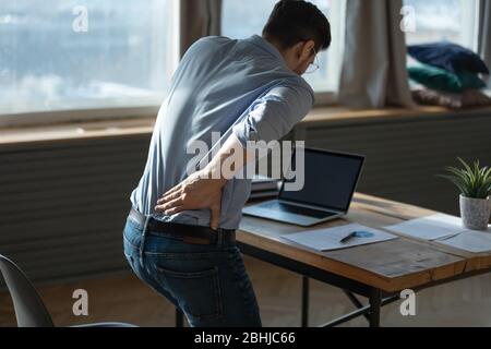 Rückansicht junger Mann, der an plötzlichen Rückenschmerzen am Arbeitsplatz leidet Stockfoto