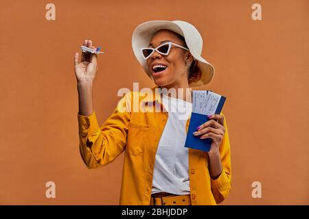 Glückliche Dame im Hut mit Sonnenbrille mit einem Flugzeug mit einem Pass mit Tickets. Stockfoto