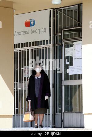 Belgrad, Serbien. April 2020. Frau mit einer schützenden Gesichtsmaske steht während der anhaltenden Pandemie der COVID-19-Krankheit vor der in kyrillischen Briefen geschriebenen 'Apotheke Belgrad'. Stockfoto