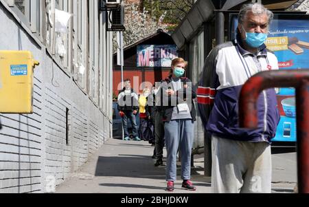 Belgrad, Serbien. April 2020. Personen mit einer schützenden Gesichtsmaske warten während der anhaltenden Pandemie der COVID-19-Krankheit, die durch das SARS-CoV-2-Coronavirus verursacht wird, in der Schlange, um das Postamt zu betreten. Stockfoto