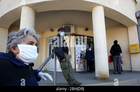 Belgrad, Serbien. April 2020. Personen mit einer schützenden Gesichtsmaske warten während der anhaltenden Pandemie der COVID-19-Krankheit, die durch das SARS-CoV-2-Coronavirus verursacht wird, in der Schlange, um das Postamt zu betreten. Stockfoto