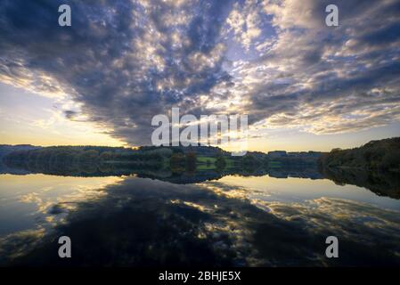 Ein großes Band dunkler Wolken überquert den Himmel und spiegelt sich auf der Oberfläche eines Flusses. Stockfoto