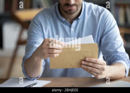 Fokussierter Geschäftsmann liest Brief, hält Umschlag in den Händen nah an Stockfoto