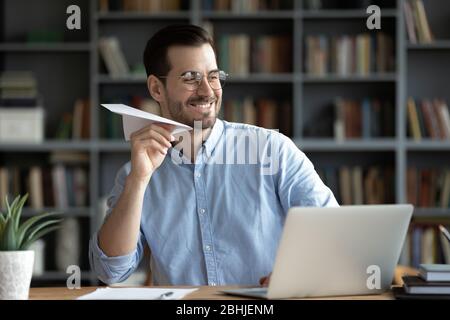 Glücklich lächelnder Geschäftsmann, der mit Papierflugzeug am Arbeitsplatz spielt Stockfoto