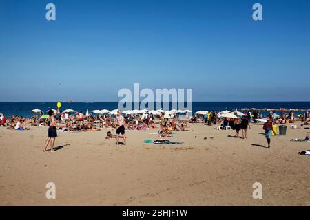 Blick auf viele Menschen, die sich auf Sand legen, sich sonnen und zwei Männer spielen am berühmten Strand "La Barceloneta" in Barcelona. Es ist ein sonniger Sommer Stockfoto