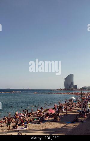 Blick auf viele Menschen, die sich auf Sand legen und sich am berühmten Strand 'La Barceloneta' in Barcelona sonnen. Das berühmte Hotelgebäude ist in der Aussicht. Stockfoto