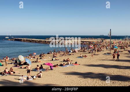 Blick auf viele Menschen, die sich auf Sand legen, sich am berühmten Strand 'La Barceloneta' in Barcelona sonnen. Es ist ein sonniger Sommertag Stockfoto