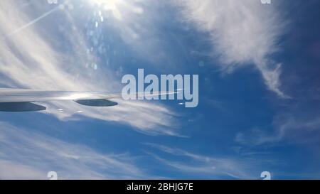 Grenzenloser blauer Himmel und hängende weiße Wolken über und unter fliegenden Flugzeug Flügel Spitze Blick von Liner Bullauge Stockfoto