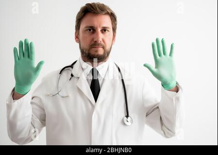 Portrait des Arztes mit Stethoskop in medizinischer Uniform zeigt beide Hände mit medizinischen Handschuhen auf einem weißen isolierten Hintergrund Stockfoto