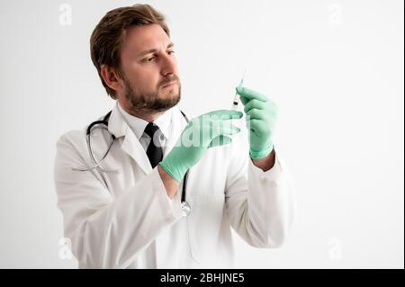 Porträt des männlichen Arztes mit Stethoskop in medizinischer Uniform mit medizinischem Handschuh und Spritze in der Hand, die auf einem weißen isolierten Hintergrund posiert Stockfoto